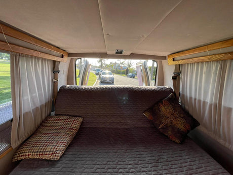 RV rental's cozy interior: a comfortable bed offers a view out open doors to a sunny, tree-lined street.