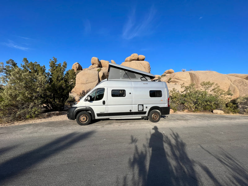 White Winnebago Solis RV rental with pop-top extended, parked among desert rocks and vegetation under a bright blue sky. — photo 11