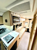 Inside this modern rv rental, find a light-toned interior with kitchen (sink, cooktop), microwave, and quilted bench seating.