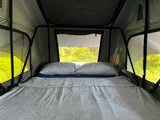 A comfy bed inside a modern roof-top tent, perfect for an rv rental adventure amidst green nature.