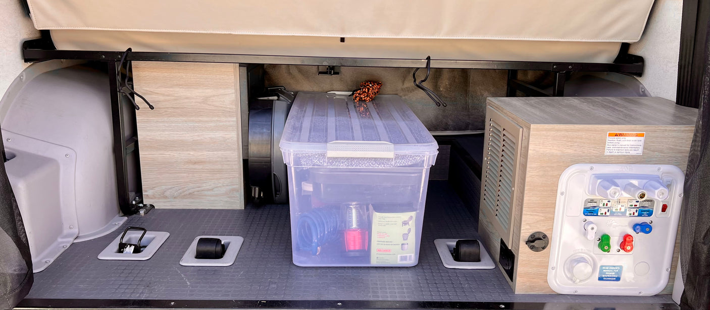 RV rental storage area featuring a water utility panel, clear bin with gear, and floor tie-downs for secure travel.