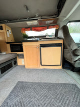 Cozy RV rental interior: microwave, mini-fridge, sink, and comfy seating. Perfect camper van setup for road trips.