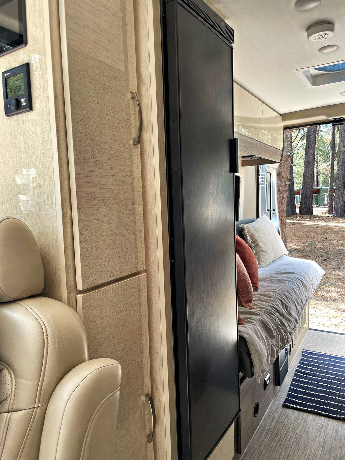 Cozy rv rental interior featuring a bed, fridge, and seating, looking out to a serene forest. Perfect for your next adventure!