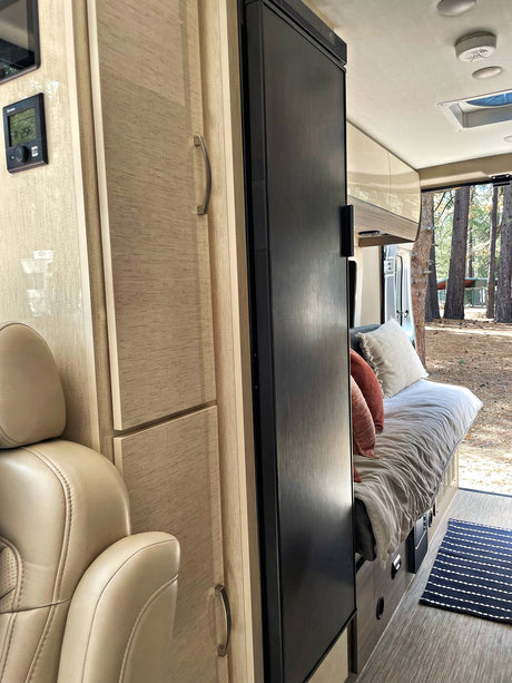 Cozy rv rental interior featuring a bed, fridge, and seating, looking out to a serene forest. Perfect for your next adventure!