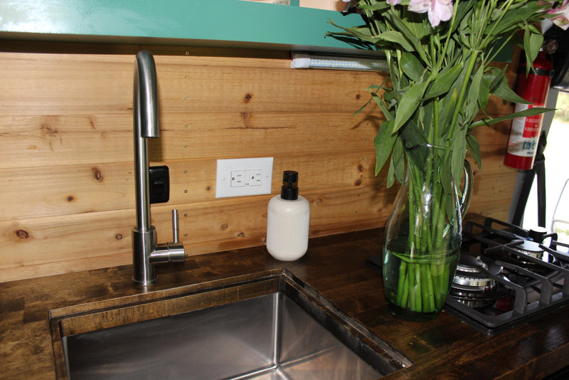 RV rental kitchen counter with stainless sink, faucet, and gas cooktop. Fresh flowers add charm to this compact space. — photo 6