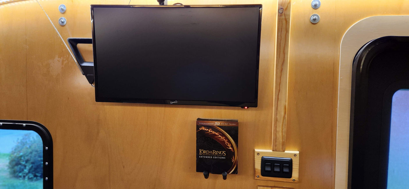 RV rental interior: A TV mounted on wood, Lord of the Rings Blu-rays below, and control switches to the right.