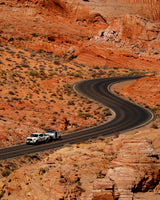 A white truck tows an RV rental through stunning red rock desert on a winding road, ideal for scenic drives and adventures.