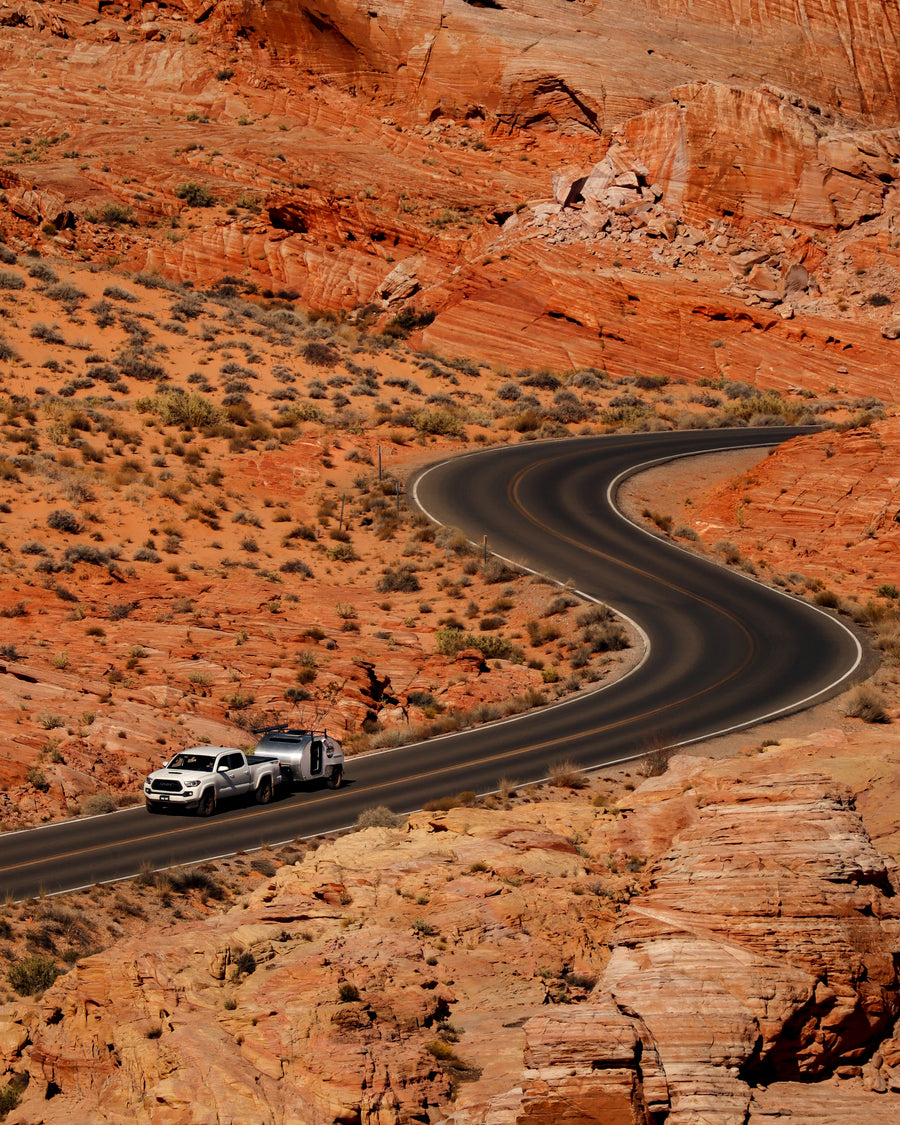 A white truck tows an RV rental through stunning red rock desert on a winding road, ideal for scenic drives and adventures.