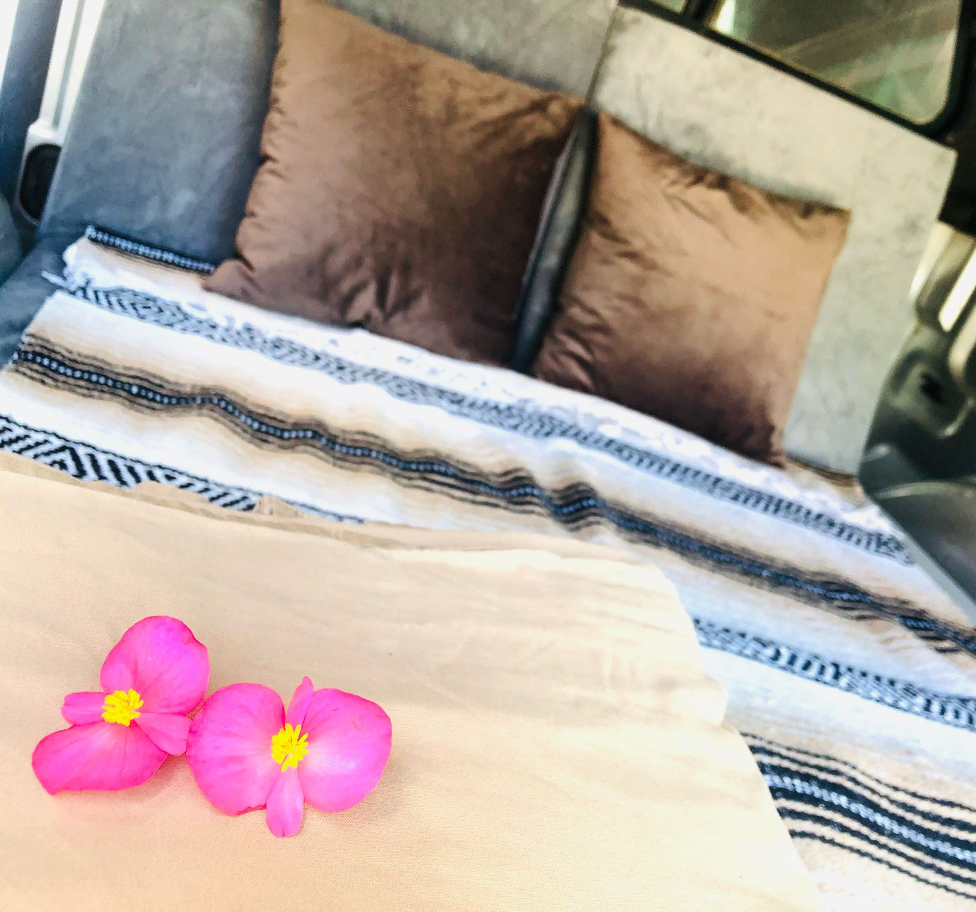 Comfortable RV rental bed featuring a patterned blanket, brown pillows, and two vibrant pink flowers.