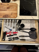 RV rental kitchen setup: Open drawer with organized utensils (spatulas, whisk, measuring spoons); countertop has induction cooktop & cutting board.