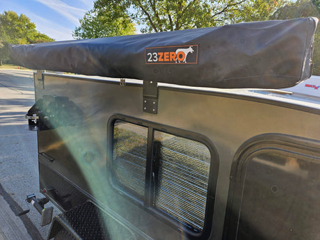 Side of a compact RV rental, showcasing a 23ZERO awning and window, perfect for outdoor camping adventures.