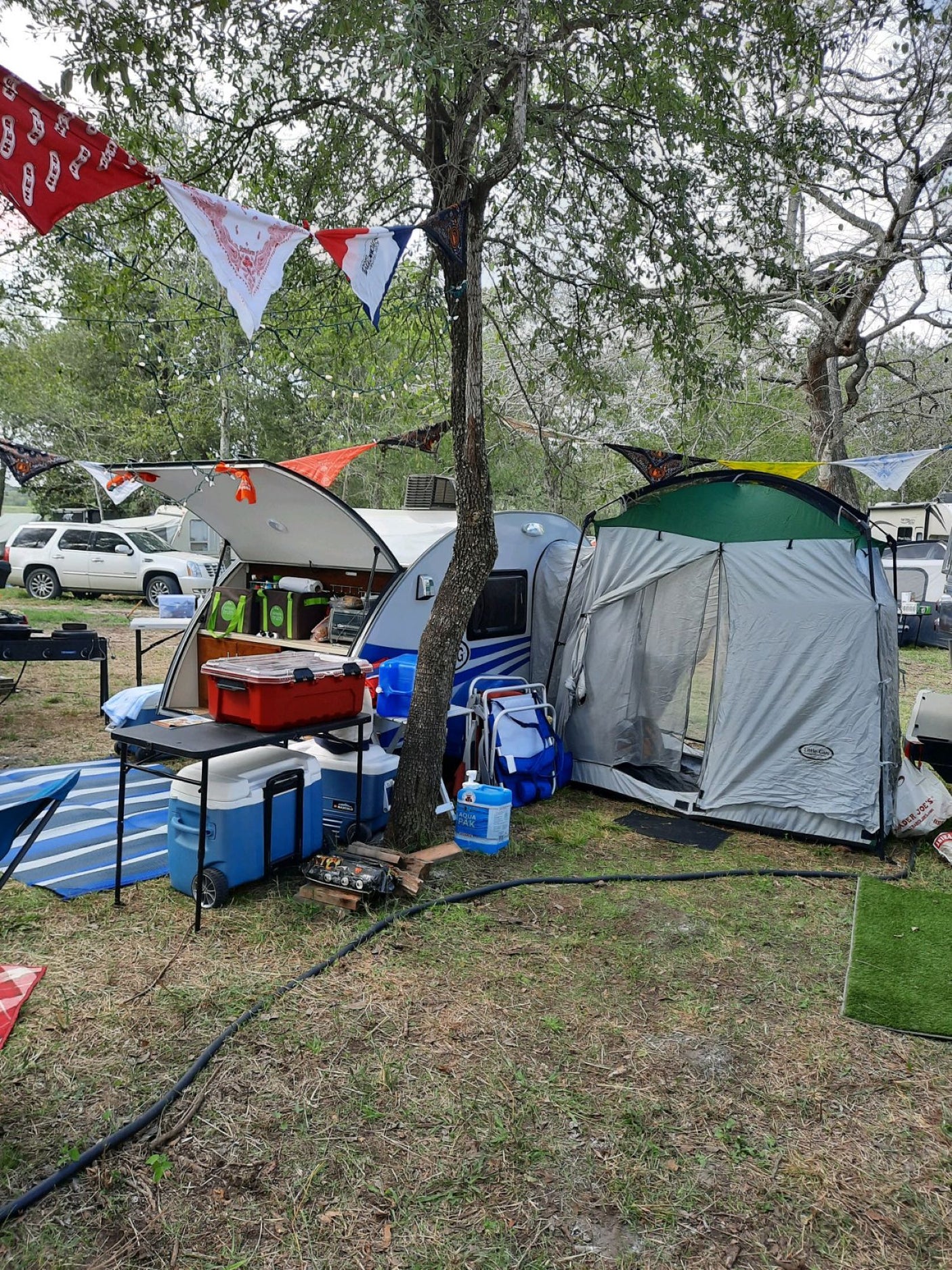 This RV rental camping setup features a teardrop trailer with an attached tent, showing a full outdoor living space.