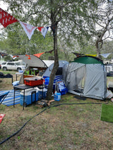 This RV rental camping setup features a teardrop trailer with an attached tent, showing a full outdoor living space.