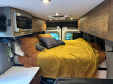 Cozy RV rental interior features a comfortable bed, microwave, and overhead cabinets.