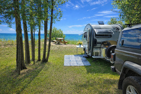 Enjoy a beautiful rv rental camping experience! A teardrop camper and SUV are parked by a sandy beach, blue ocean, and trees.