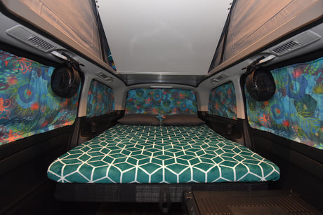 Cozy RV rental camper van interior featuring a pop-top, custom ocean-themed curtains, and a geometric-patterned bed.
