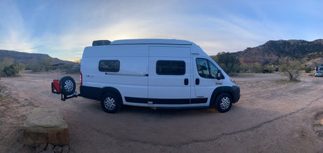 This Winnebago Solis RV rental is perfectly parked at a scenic desert campsite, surrounded by mountains under a clear sky.