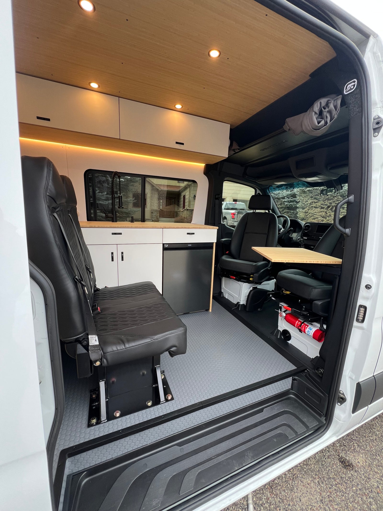 Clean, modern RV rental interior featuring a custom kitchen with fridge, cozy seating, wood ceiling, and safety equipment.