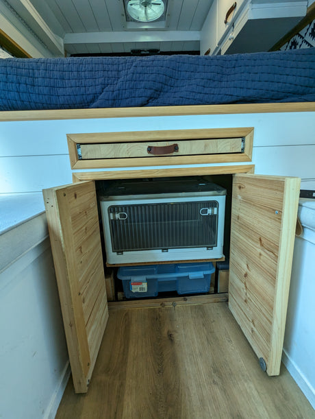 Compact RV rental interior featuring a bed, pull-out drawer, and portable fridge with storage.