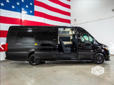 Black luxury conversion van, ideal for RV rental. Its open side door reveals a custom interior, set against an American flag.
