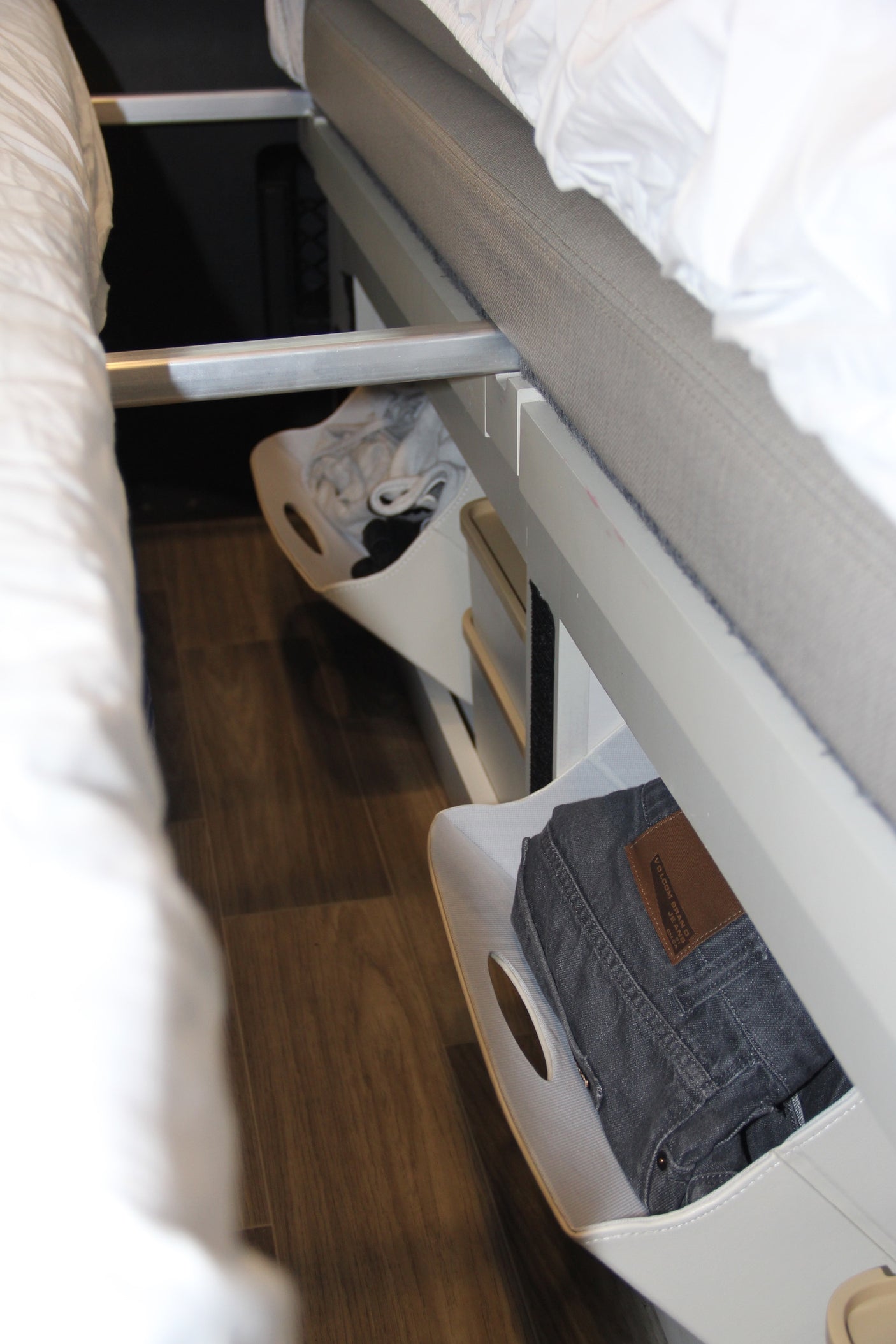 RV rental smart under-bed storage: white bins with clothes, including Volcom jeans, and shoes on a wooden floor.