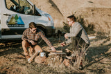 Two men prepare a campfire next to a Wandervans RV rental, ready for an outdoor adventure in their camper van.
