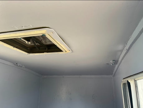 RV rental interior: a light gray ceiling with a central roof vent and a side window, providing natural light.