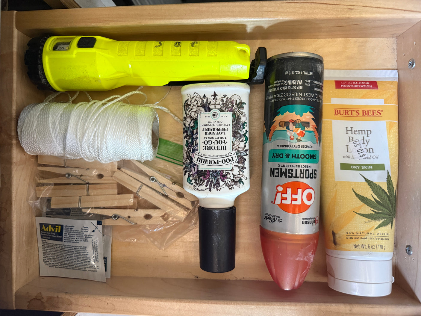 RV rental drawer packed with essentials: flashlight, string, clothespins, Advil, Poo-Pourri, bug spray, and lotion.