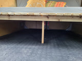 RV rental camper bed frame and storage area: A wooden slatted bed platform with a central support leg over a black rubber floor.