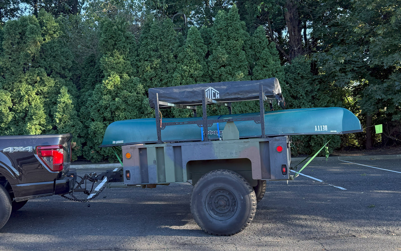 A pickup truck tows a camouflage utility trailer with a canoe and rooftop tent, an alternative for your rv rental camping trip.