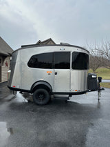 Stylish Airstream Basecamp travel trailer, silver with black accents, on wet driveway. Ideal for rv rental adventures.