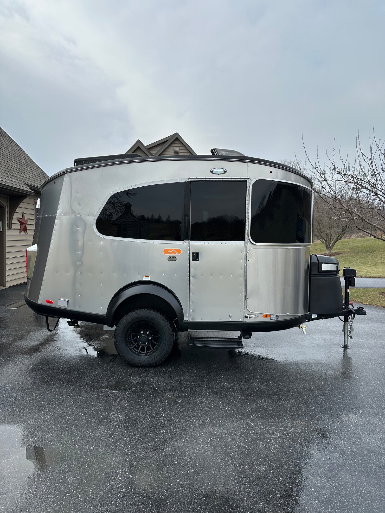 Stylish Airstream Basecamp travel trailer, silver with black accents, on wet driveway. Ideal for rv rental adventures.