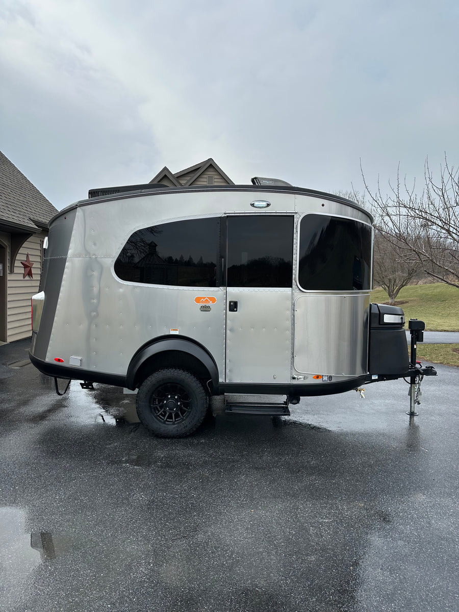 Stylish Airstream Basecamp travel trailer, silver with black accents, on wet driveway. Ideal for rv rental adventures.