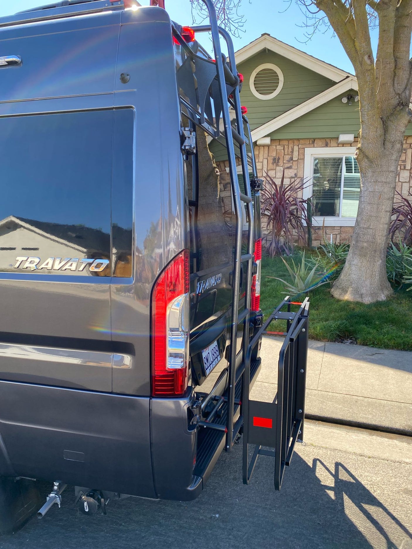 Grey Travato RV rental's rear, featuring a ladder and folding cargo carrier. Ideal for travel & extra gear.