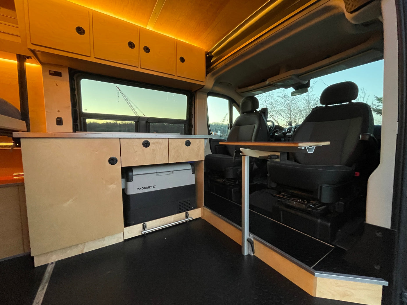 This RV rental offers a spacious camper van interior with a kitchen, Dometic fridge, and swiveling front seats with a table. — photo 6