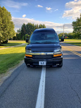Front view of a sleek black high-top conversion van, ideal as an RV rental, parked on a road with a center line.