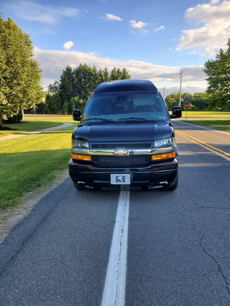 Front view of a sleek black high-top conversion van, ideal as an RV rental, parked on a road with a center line.