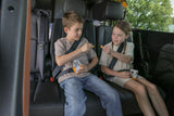 Two children, a boy & girl, safely belted and snacking in an rv rental, enjoying the backseat view on their journey.