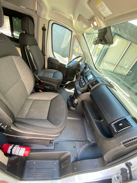 Front cabin of an RV rental, showing driver and passenger seats, dashboard, and a fire extinguisher for safety.