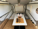 This RV rental's inviting interior features a dining table with chess & snacks, beds, and charging outlets.