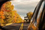 Side mirror view of an overlanding vehicle with a rooftop tent on a fall road, perfect for your next RV rental adventure.
