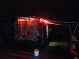 Experience an RV rental van at night, illuminated by brilliant red lights from its rear and extended awning. Ready for adventure!