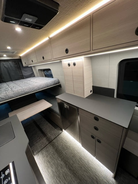 Modern RV rental interior: galley kitchen, overhead storage, and comfortable sleeping area.