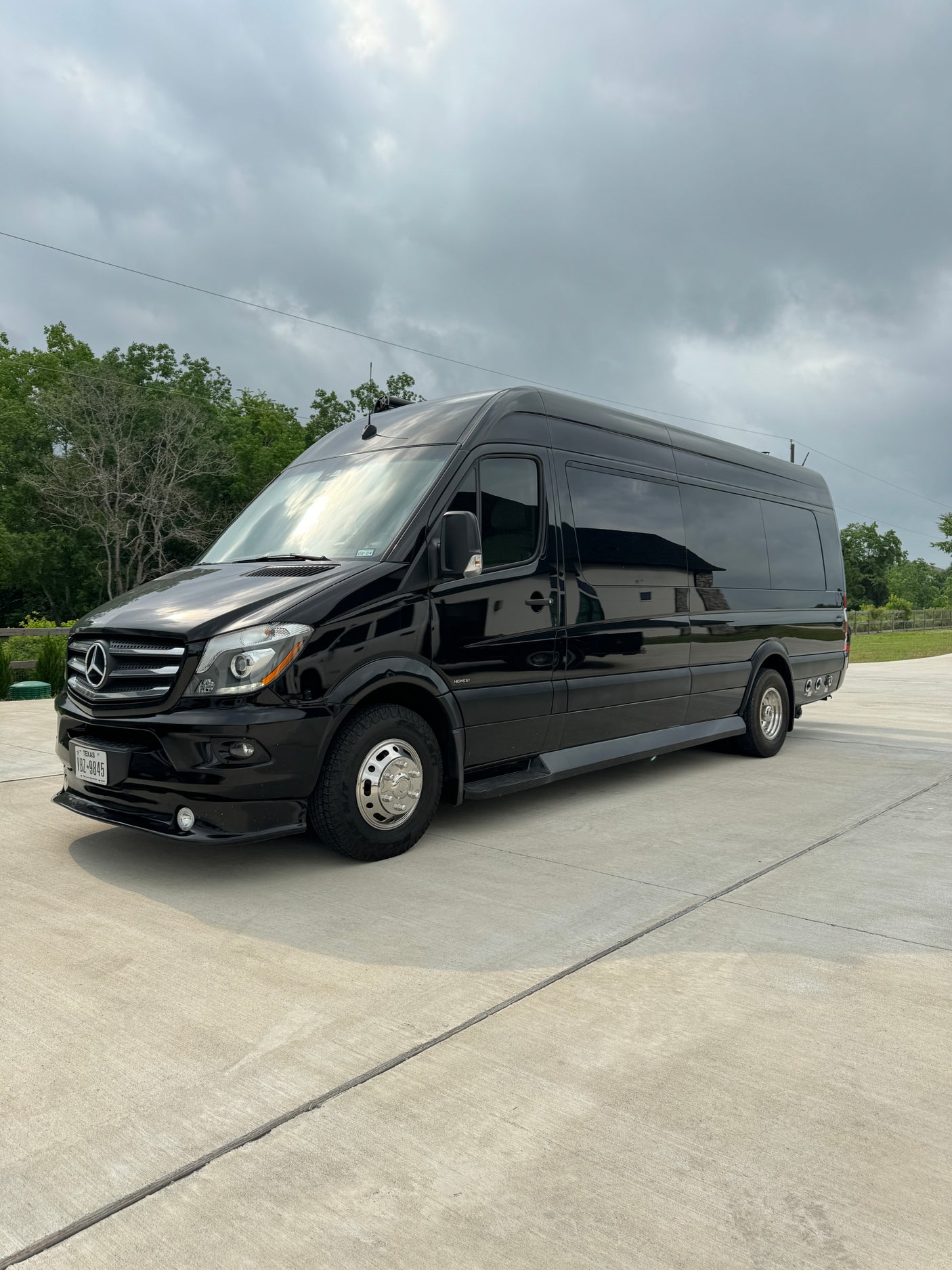 Black Mercedes-Benz Sprinter luxury RV rental van parked on concrete under an overcast sky.