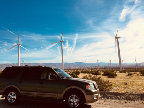 A dark SUV at a desert wind farm under blue skies. Ideal for road trips! Think RV rental for your next adventure.