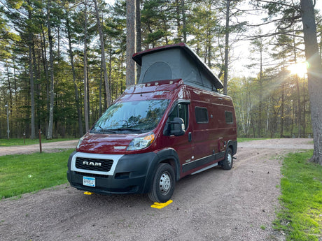 This RV rental in a serene wooded campsite features a red pop-top camper van ready for adventure.