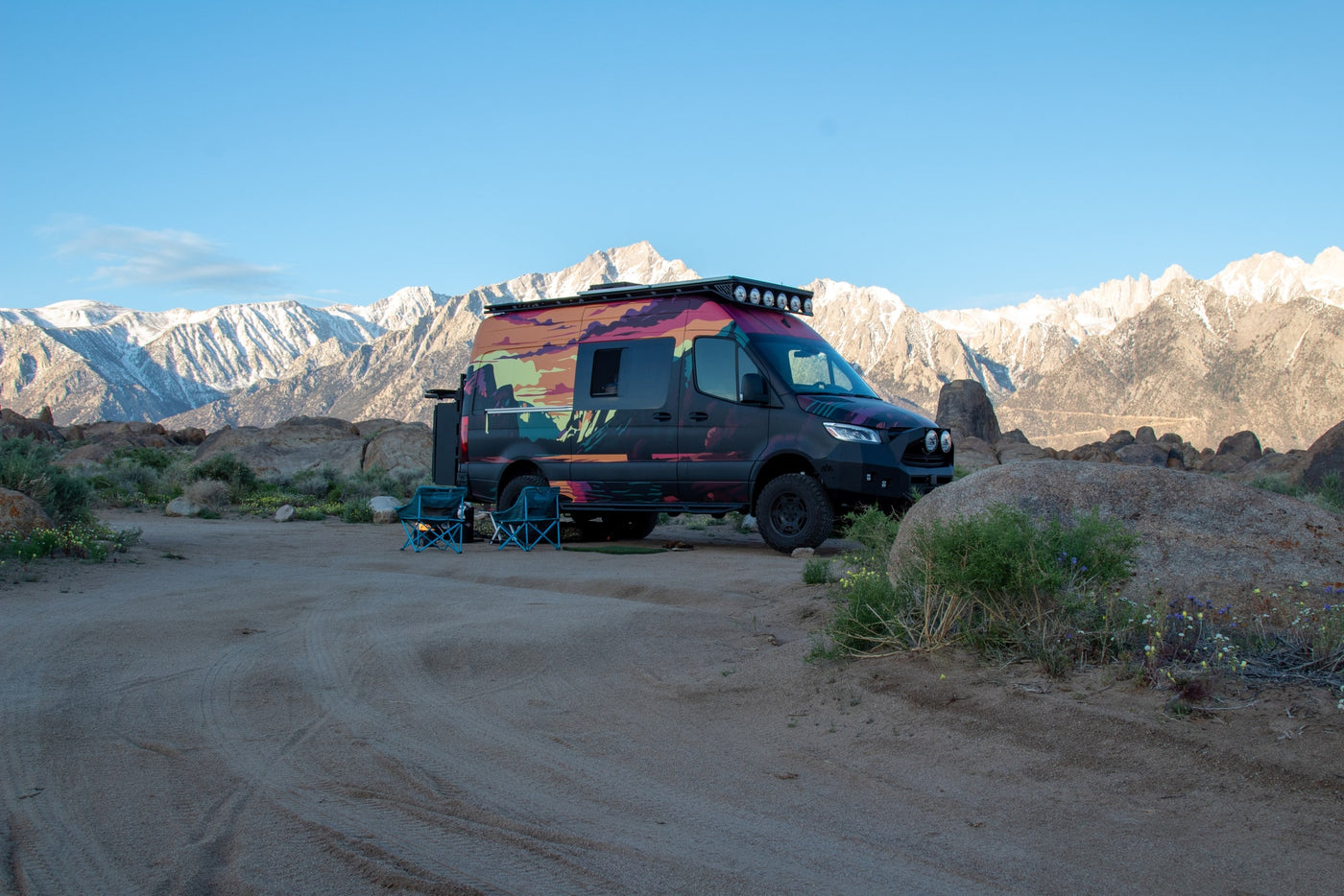  foregrounded by chairs and snow-capped mountains.|Experience off-grid camping! This colorful RV rental van is parked with chairs amidst rocks — photo 5