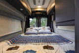Experience comfort in this RV rental bedroom with fishing-themed quilt & pillows. Enjoy forest views from your camper van.