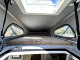 Interior view of a spacious pop-top roof bed in an rv rental camper van. Enjoy elevated sleeping with large side and sky windows.