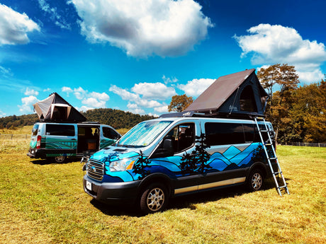 Two customized RV rental camper vans with rooftop tents in a scenic field under a blue sky.